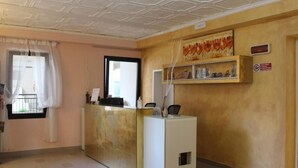 Un espace d’accueil comprenant un comptoir de réception, une fenêtre avec des rideaux, une étagère murale agrémentée d’objets décoratifs et un panneau indiquant qu’il est interdit de fumer.