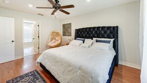 Quarto com cama grande, ventilador de teto, porta branca e cadeira de vime.