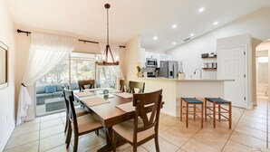 Cozinha moderna com armários brancos, uma ilha central e uma área de refeições com mesa e cadeiras de madeira.