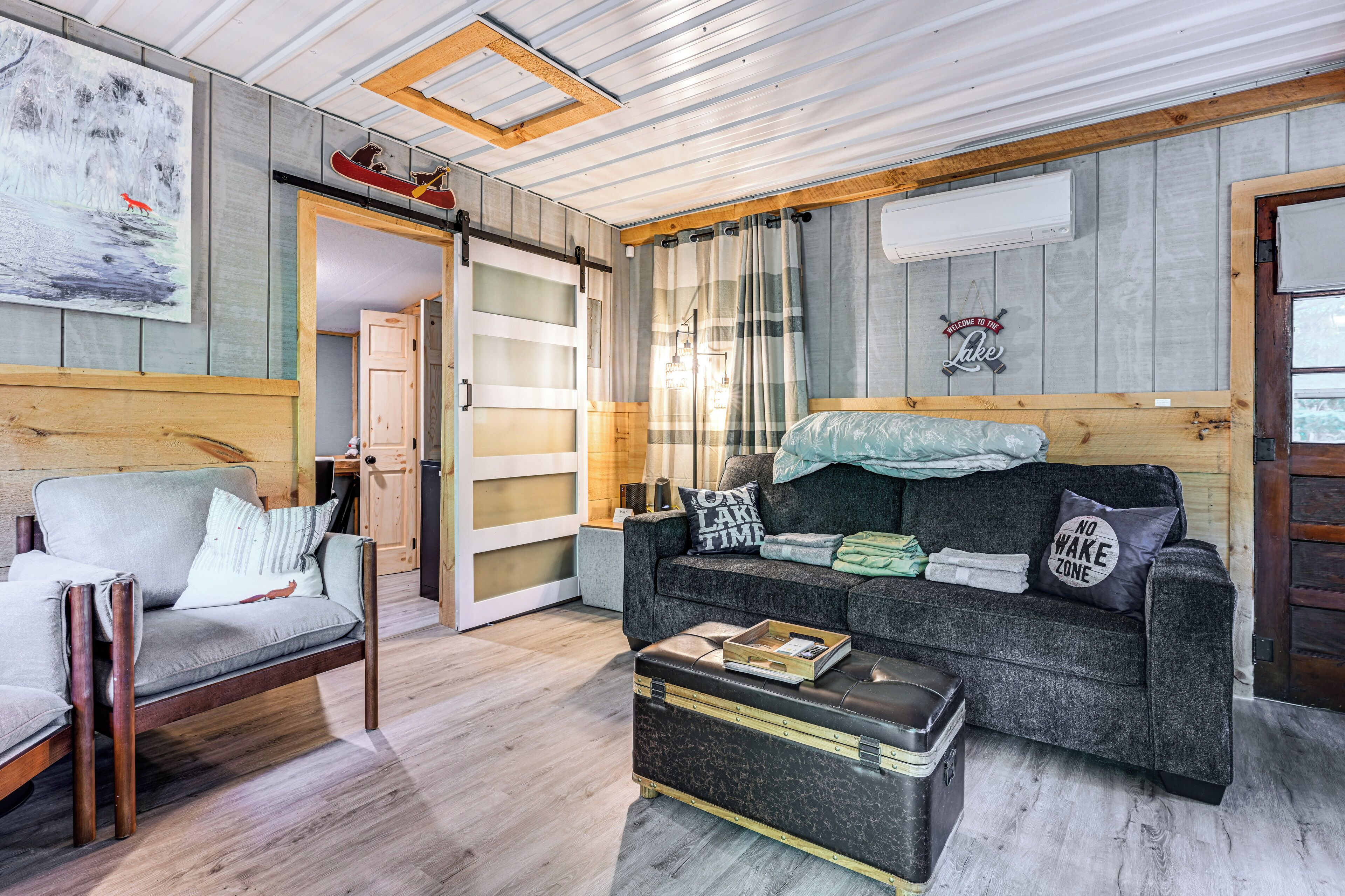 Un salon chaleureux avec un canapé gris, une chaise en bois et une petite table sur laquelle se trouve une valise.