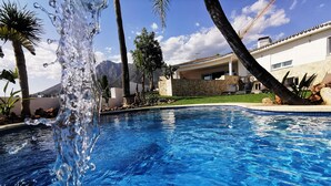 Ein Schwimmbecken mit klarem Wasser, umgeben von Palmen und einem Haus mit Steinverkleidung.