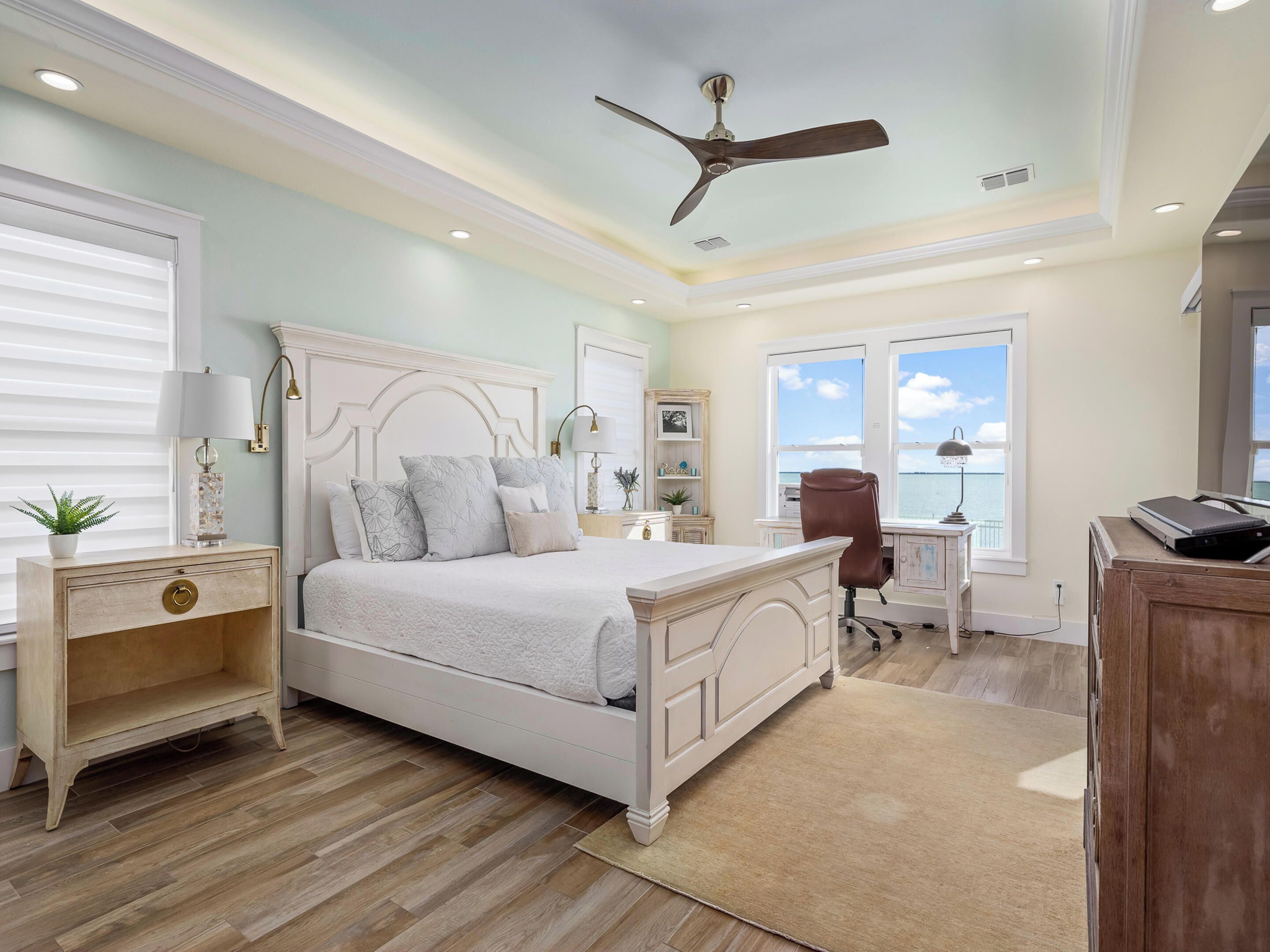 A bedroom with a large bed, a desk, a chair, and a view of the ocean.