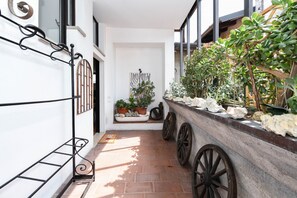 Un couloir étroit avec un mur blanc, un banc en bois, des plantes en pot et un élément décoratif mural.