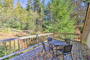 A wooden deck with a table and chairs, overlooking a forested area.