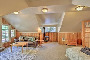 Une pièce mansardée chaleureuse, avec un plafond en pente, un poêle à bois, un canapé, une table basse et un lit.