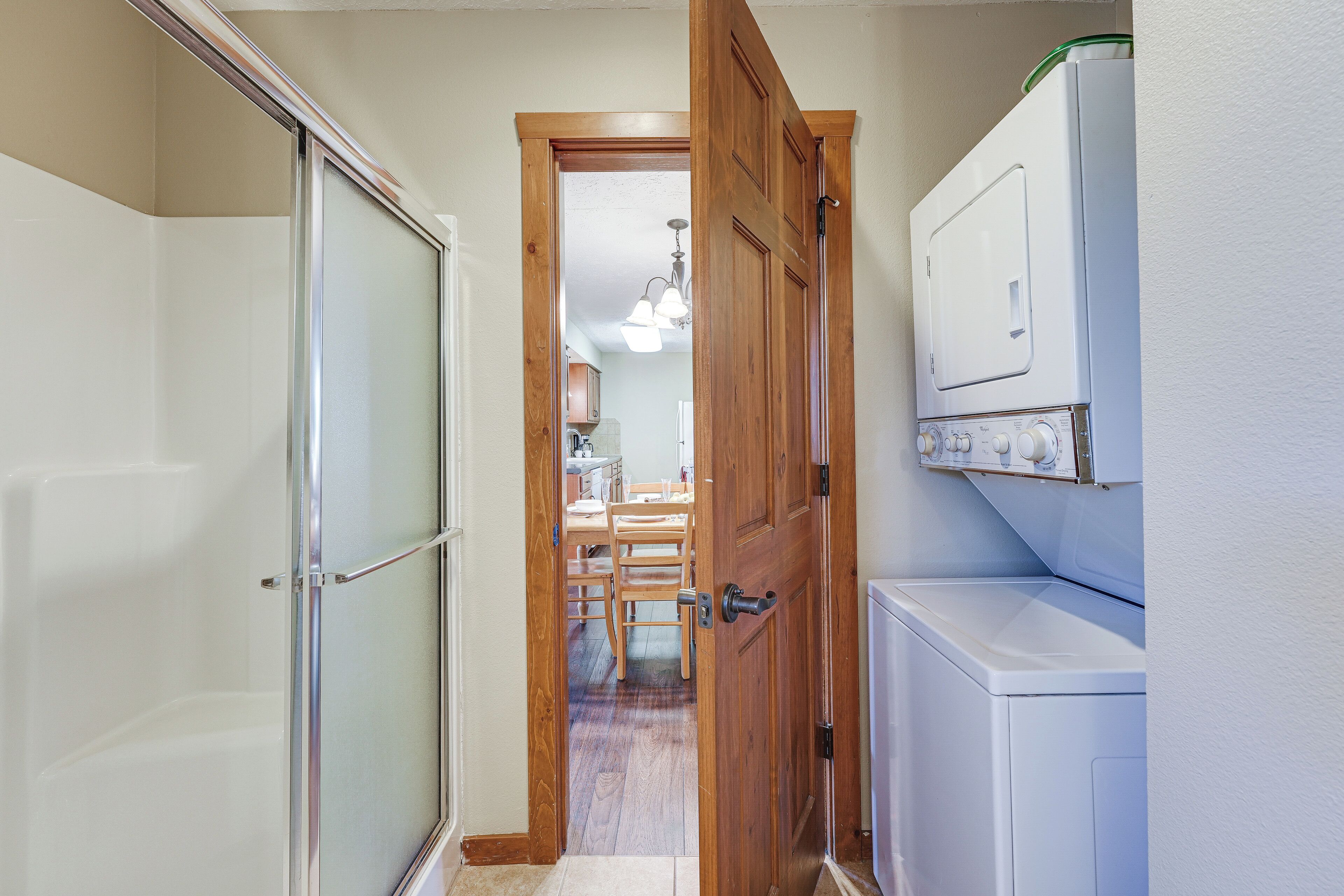 A laundry room with a washing machine, a dryer, and a wooden door leading to a dining area.