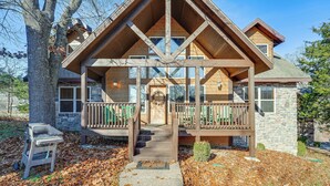 A two-story log cabin with a stone foundation, a wooden deck, and a front porch. - Families Welcome! Branson Resort-style Getaway (Branson)
