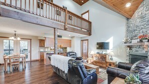 A spacious living room with a large leather sofa, a dining area with wooden furniture, a stone fireplace, and a high ceiling with exposed beams. - Families Welcome! Branson Resort-style Getaway (Branson)