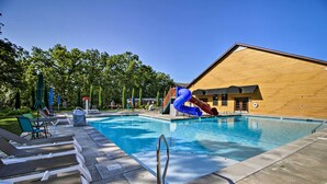 A pool area with lounge chairs, a slide, and a wooden building in the background. - Families Welcome! Branson Resort-style Getaway (Branson)