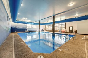 An indoor swimming pool with clear water, a tiled floor, and a mural on the wall depicting mountains.