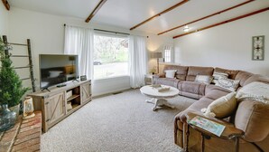 Ett vardagsrum med en tv, en soffa, ett soffbord och ett fönster med gardiner.
