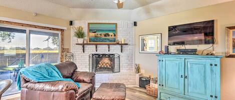 A living room with a fireplace, leather sofa, ottoman, and a television mounted on the wall.