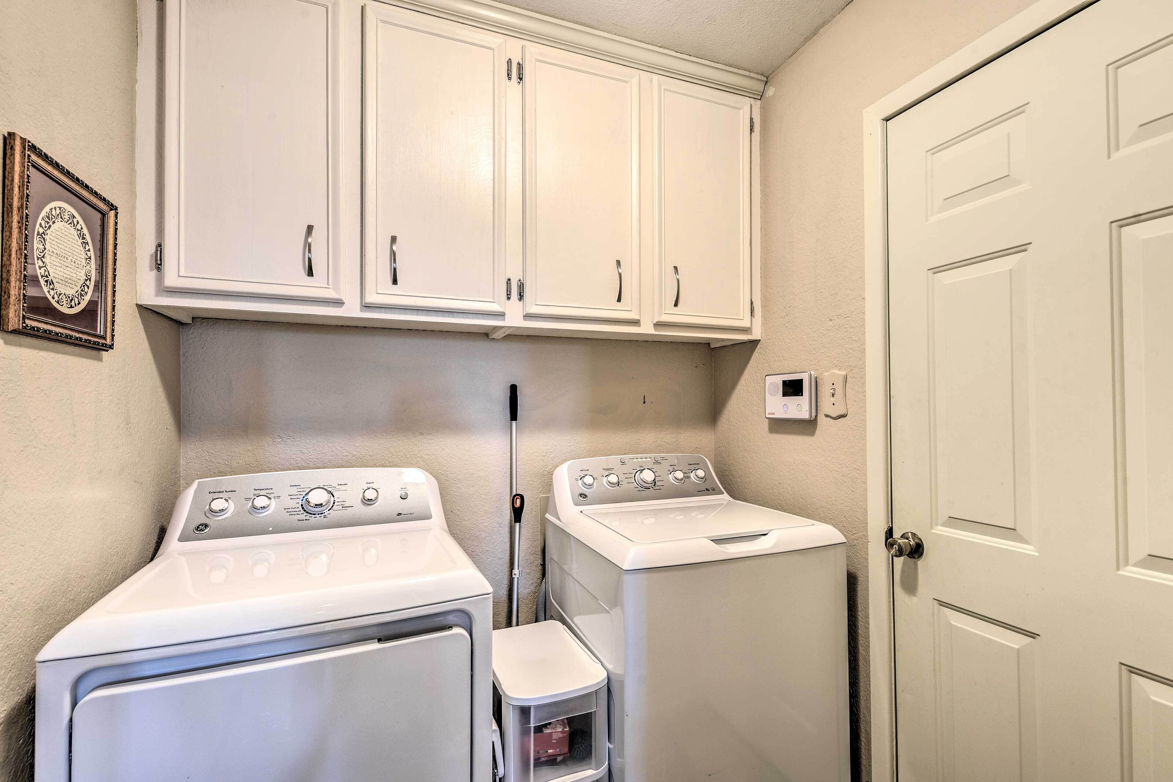 A laundry room with two white washing machines, a small trash bin, and a door.