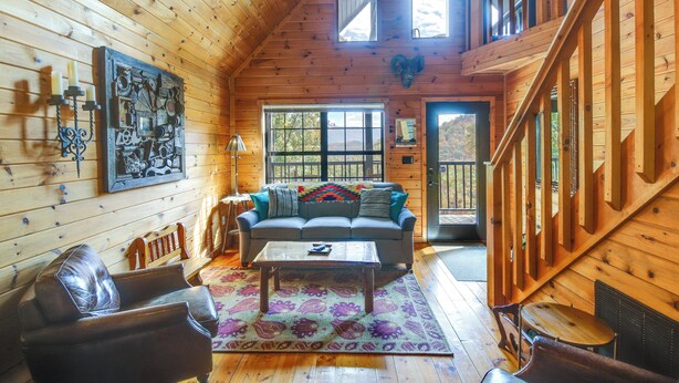 A cozy cabin interior with wooden walls, a sofa, a coffee table, and a staircase. - Prime Views! Above & Beyond Pigeon Forge Cabin (Sevierville)