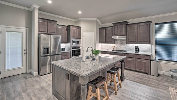 A modern kitchen with granite countertops, stainless steel appliances, and dark wood cabinets. - Aledo Home: Covered Patio & Yard, Near Fort Worth! (Aledo)