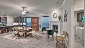 A spacious living area with a dining table, chairs, a fireplace, and a kitchen in the background. - Aledo Home: Covered Patio & Yard, Near Fort Worth! (Aledo)