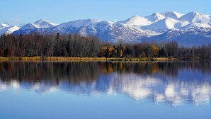 A calm lake reflecting snow-capped mountains and a forested shoreline. - Alluring Anchorage Apt - Walk to Coastal Trl! (Anchorage)