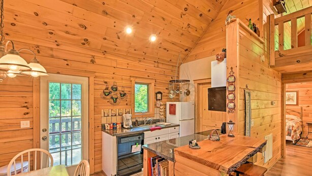A cozy cabin interior with wooden walls, a kitchen area, a dining table, and a bed. - Rustic Andrews Cabin Rental w/ Deck + Fire Pit! (Andrews)