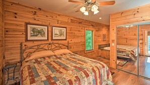 A wooden cabin bedroom with a bed, a ceiling fan, and framed pictures on the walls. - Rustic Andrews Cabin Rental w/ Deck + Fire Pit! (Andrews)