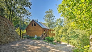 A rustic log cabin with a porch, surrounded by dense forest and a gravel driveway. - Rustic Andrews Cabin Rental w/ Deck + Fire Pit! (Andrews)