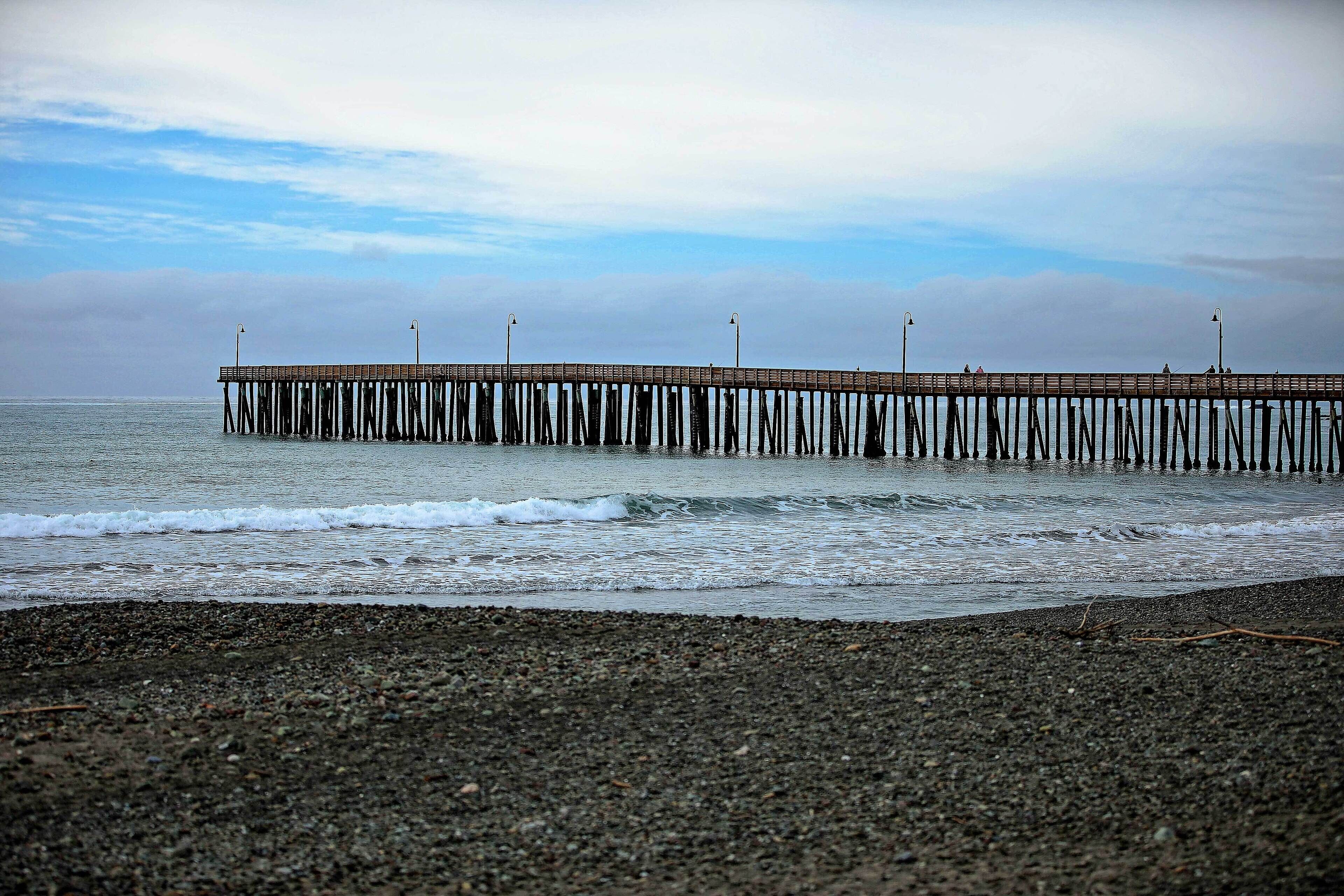 A pier extending into calm waters with a cloudy sky above.