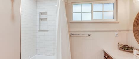 Een badkamer met een bad, douchegordijn, raam en een wastafel met lades.