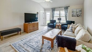A living room with a flat-screen TV, wooden cabinet, bench, sofa, coffee table, and patterned rug. - Bastrop Home w/ Yard, 28 Mi to Austin! (Bastrop)