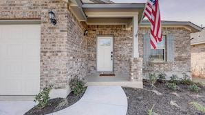 A brick house with a white garage door, a front porch, and an American flag. - Bastrop Home w/ Yard, 28 Mi to Austin! (Bastrop)