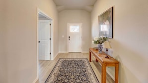 A hallway with a wooden floor, a patterned rug, a white door, and a small table with a vase of flowers and a lamp. - Bastrop Home w/ Yard, 28 Mi to Austin! (Bastrop)
