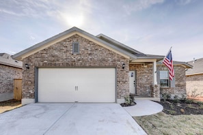 A two-story house with a brick facade, a white garage door, and an American flag. - Bastrop Home w/ Yard, 28 Mi to Austin! (Bastrop)