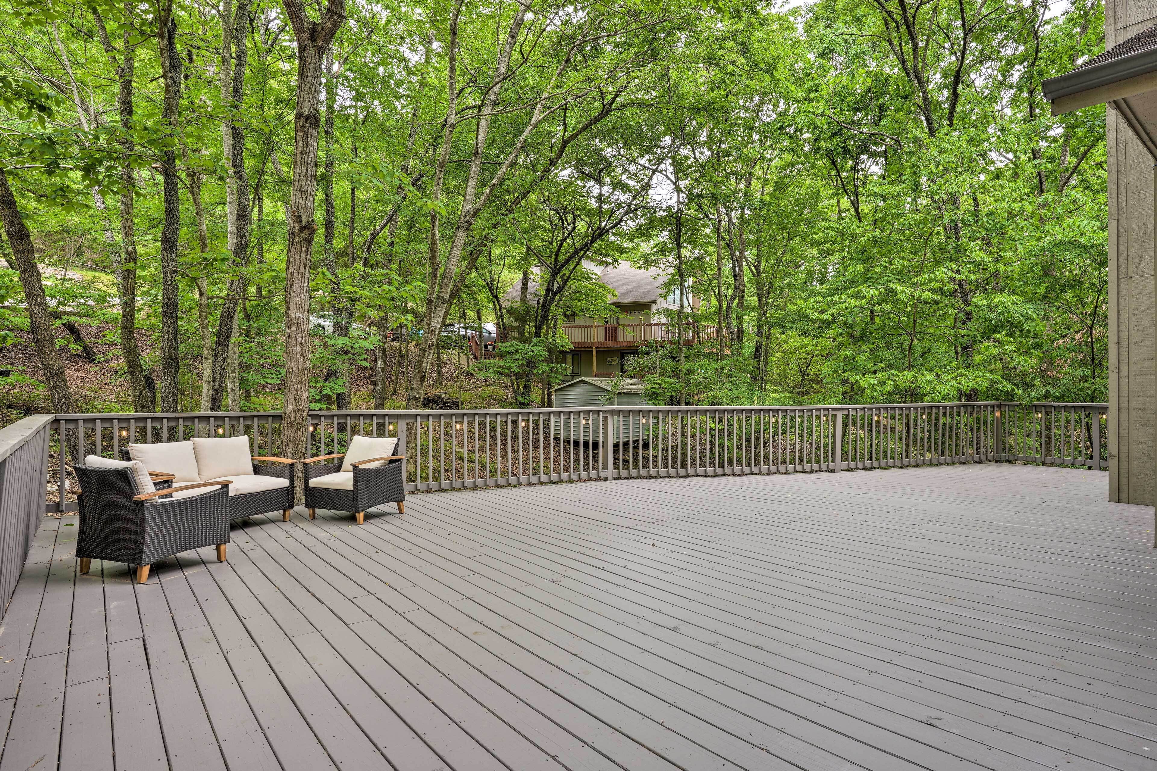 Eine Holzterrasse mit Gartenmöbeln, umgeben von Bäumen und einem Haus im Hintergrund.