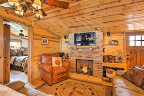 A cozy log cabin interior with a fireplace, leather furniture, and a stone wall.