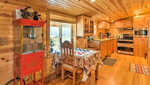 A cozy wooden cabin interior with a dining table, chairs, a popcorn machine, and a kitchen area with wooden cabinets and appliances.