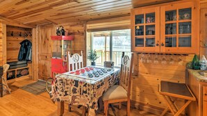 A wooden cabin interior with a dining table set for two, a red cabinet, and a glass-fronted storage unit.