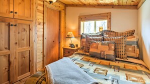 A wooden cabin-style bedroom with a bed, a nightstand, a lamp, and a window.
