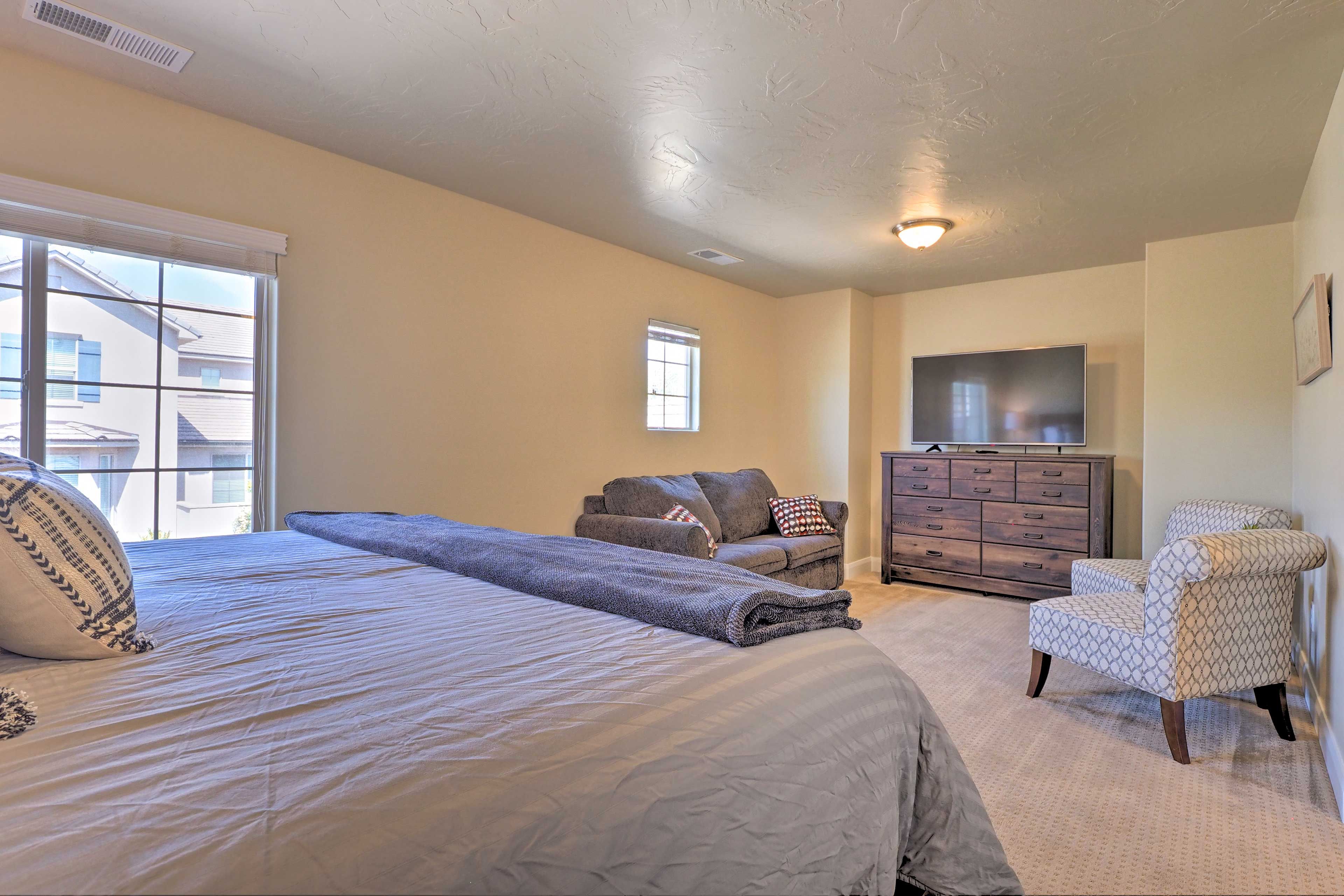 A bedroom with a large bed, a dresser, a TV, and a chair.