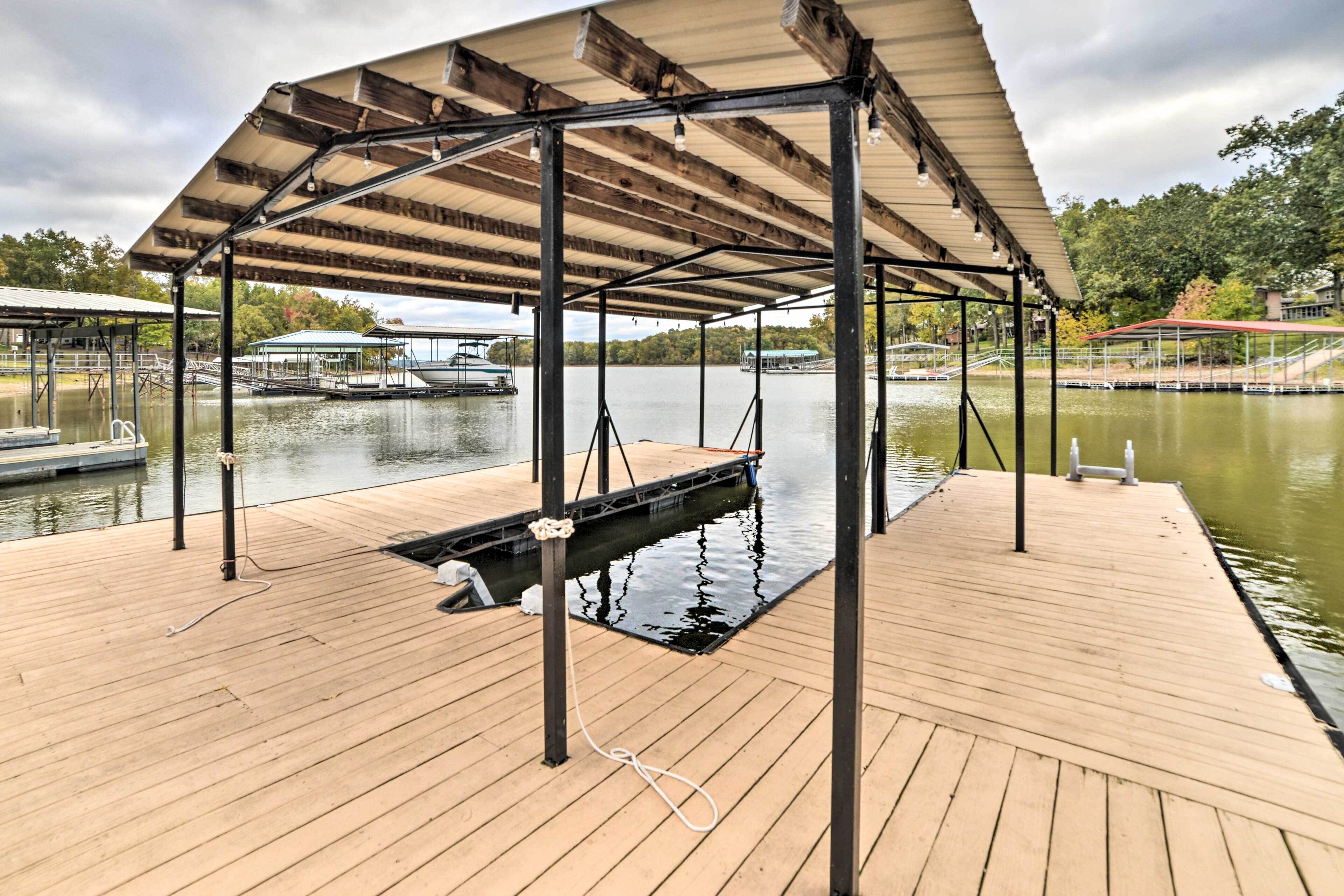 A wooden dock with a covered pavilion, a small pool, and boats in the background.