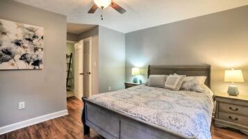 A bedroom with a bed, nightstands, a ceiling fan, a wall art piece, and a door leading to another room.