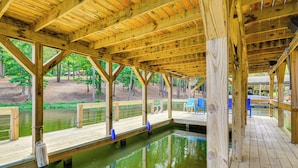 Una terraza de madera sobre el agua, con vista a árboles y un edificio distante.