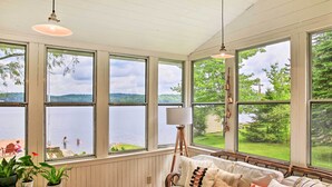 Ein gemütliches Zimmer mit großem Fenster mit Seeblick, einem Korbsessel und einer Stehlampe.