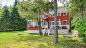 Ein rotes Haus mit weißer Veranda, umgeben von Bäumen und einem Rasen.
