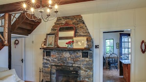 Ein gemütliches Wohnzimmer mit Kamin aus Stein, Holzbalken und einer Chandelier.