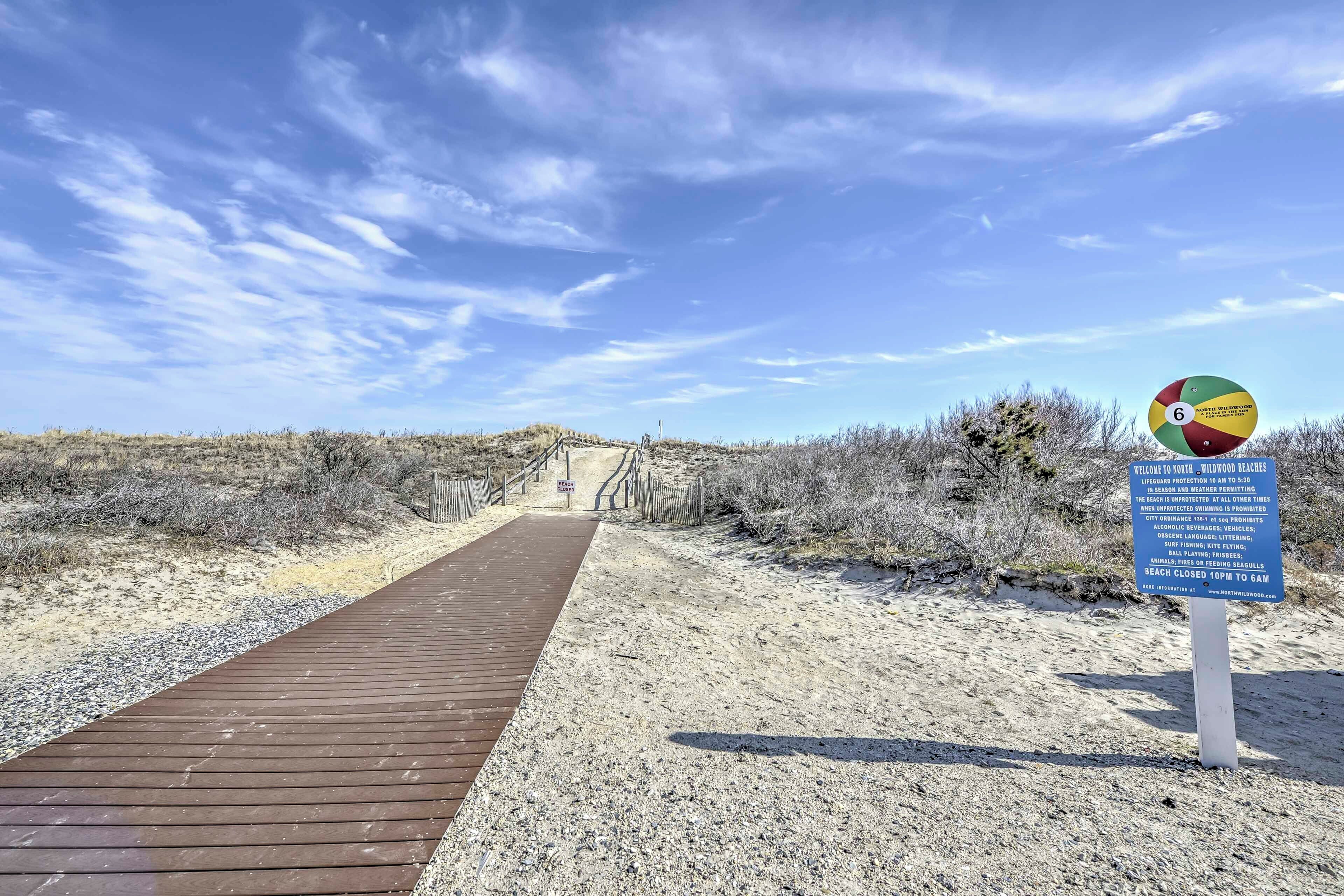 A wooden boardwalk leading to a beach area with a sign indicating beach rules and hours.