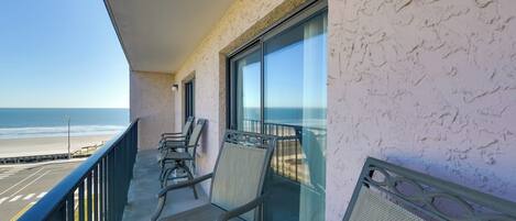 A balcony with chairs overlooking a beach.