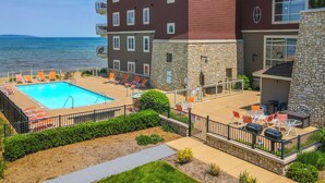 A pool area with lounge chairs and a stone building with a view of the water. - Beachfront Traverse City Resort Condo w/ Pool (Traverse City)