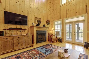 A wooden-paneled room with a fireplace, a television, a patterned rug, and a door with blinds. - Hot Tub & Mtn Views: Beautiful Bryson City Home (Bryson City)