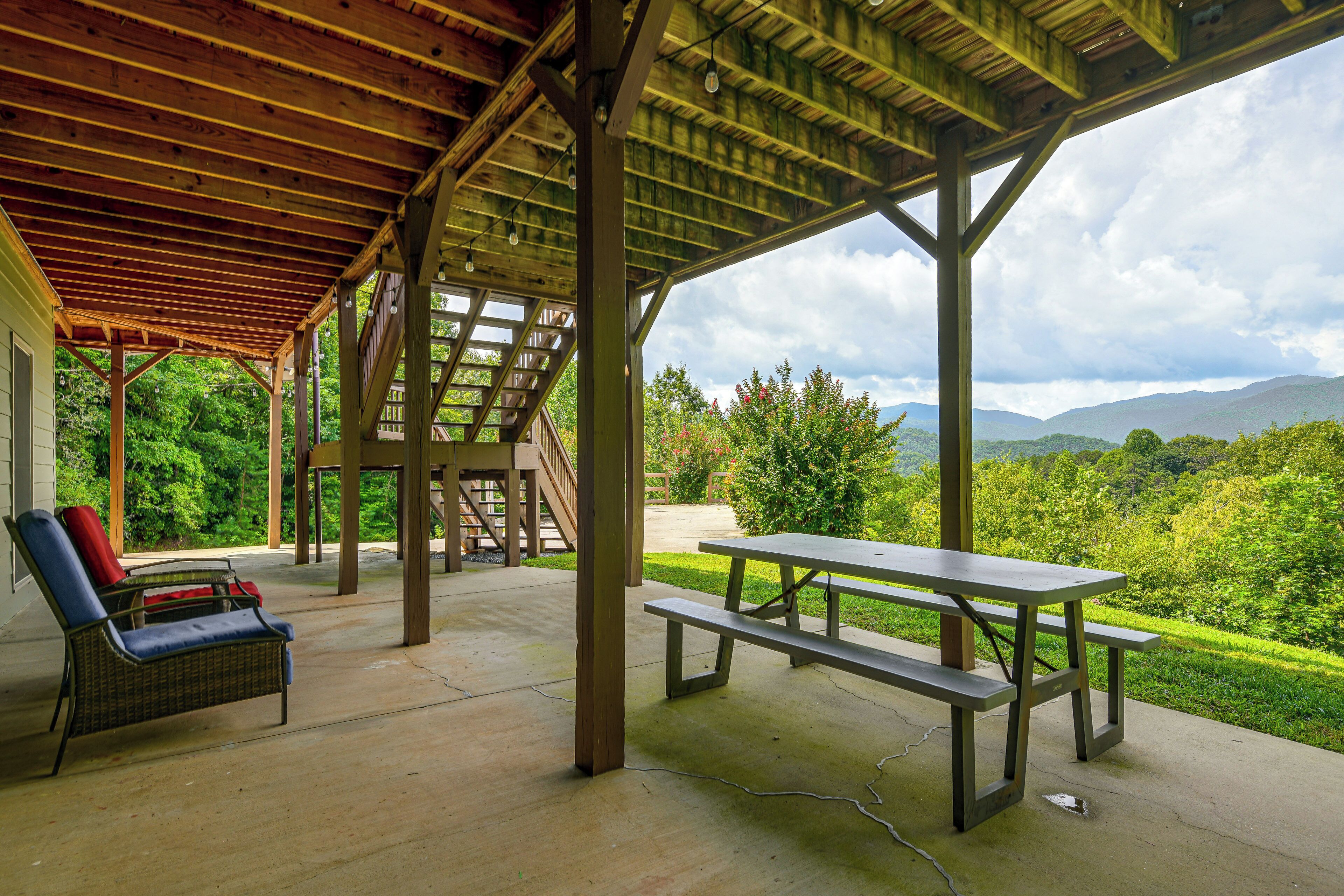 A covered outdoor area with a picnic table and chairs, a staircase, and a view of a lush landscape.