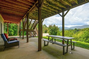 A covered outdoor area with a picnic table and chairs, a staircase, and a view of a lush landscape.