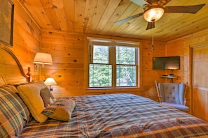 Ein Schlafzimmer einer Holzhütte mit einem Bett, einem Sessel, einem Fernseher und einem Deckenventilator.