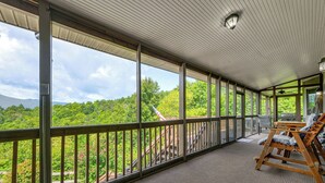 Un espacio al aire libre techado con vista a un paisaje boscoso, una terraza de madera y un área de estar con mesa y sillas.